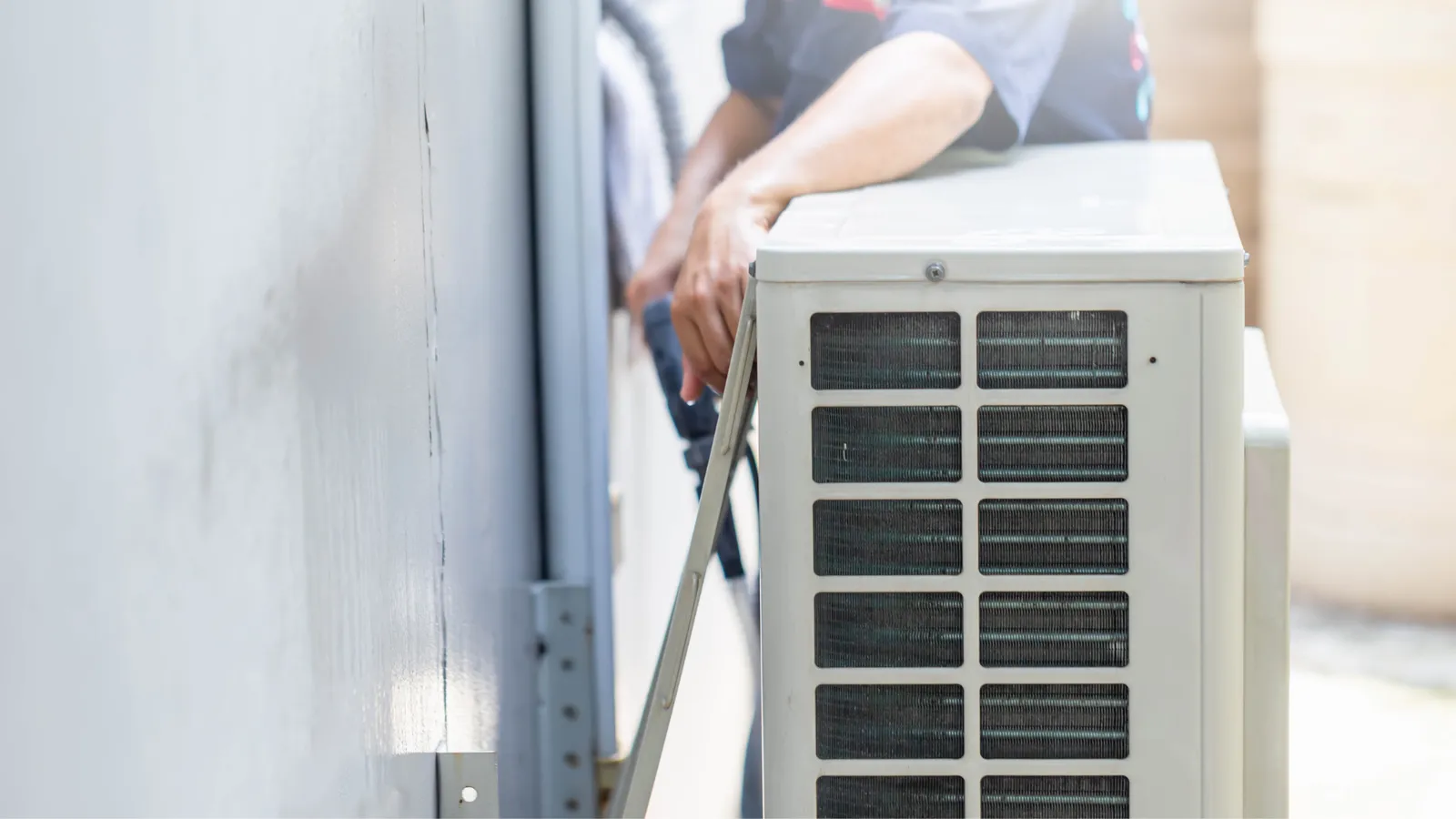 A man is installing an air conditioner on the side of a building.